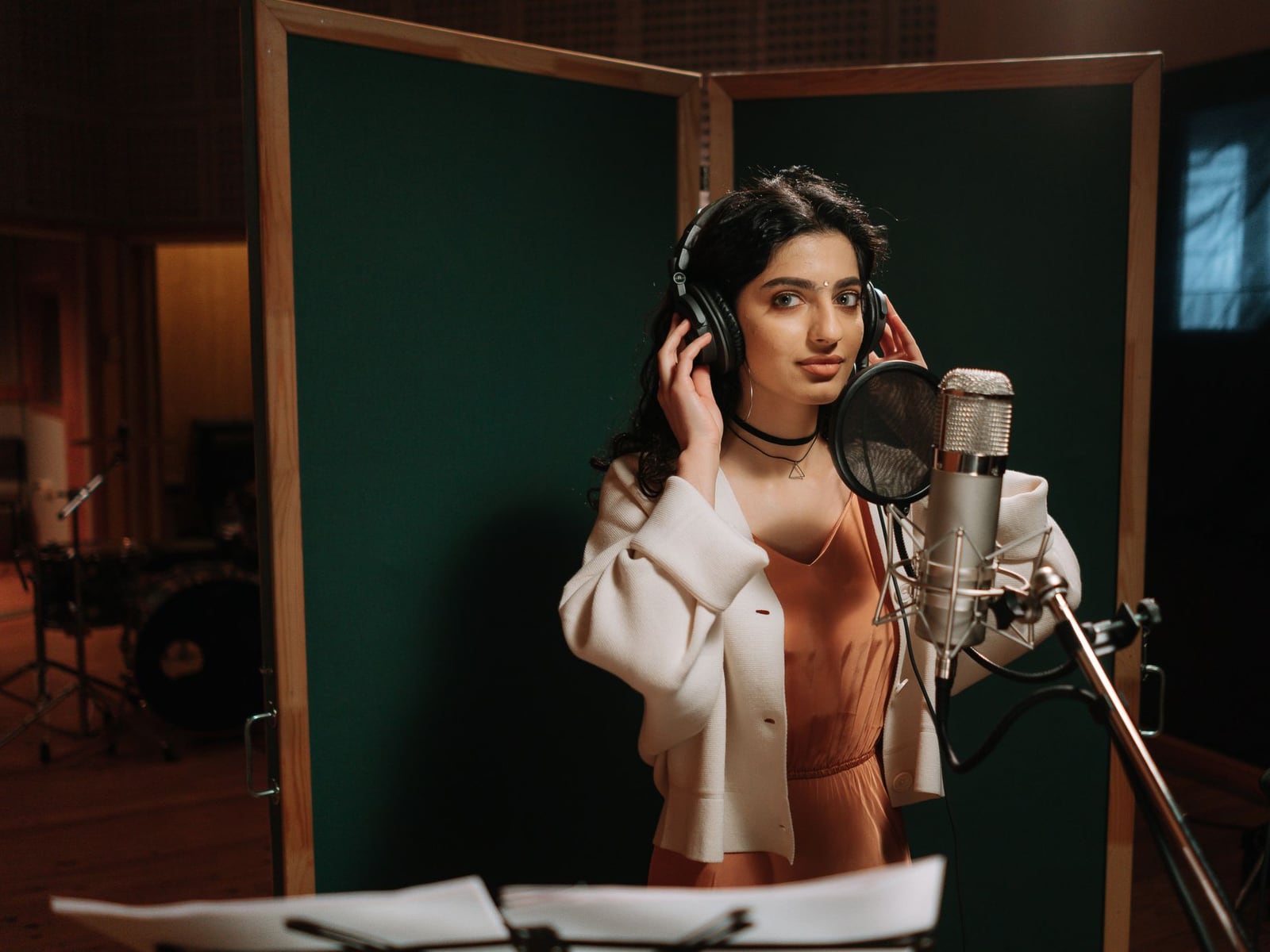 A singer recording vocals in a professional soundproof booth with a condenser microphone